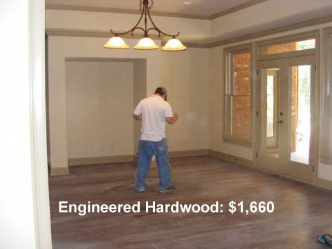 A man standing in an unfinished room with wood floors.